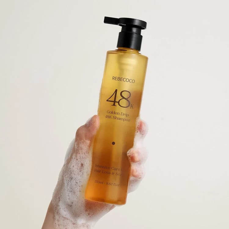 REBECOCO Golden Drip 48K Korean scalp care shampoo bottle, 255ml, held in a foam-covered hand